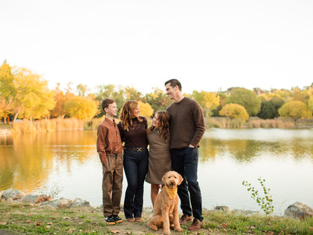 Family of four and a dog smile by a lake in autumn. Bright orange and green foliage reflects in the water, creating a warm atmosphere. Hellyer County Park in San Jose fall family photoshoot with dog by Bay Area photographers HKCreate About the Location Guide