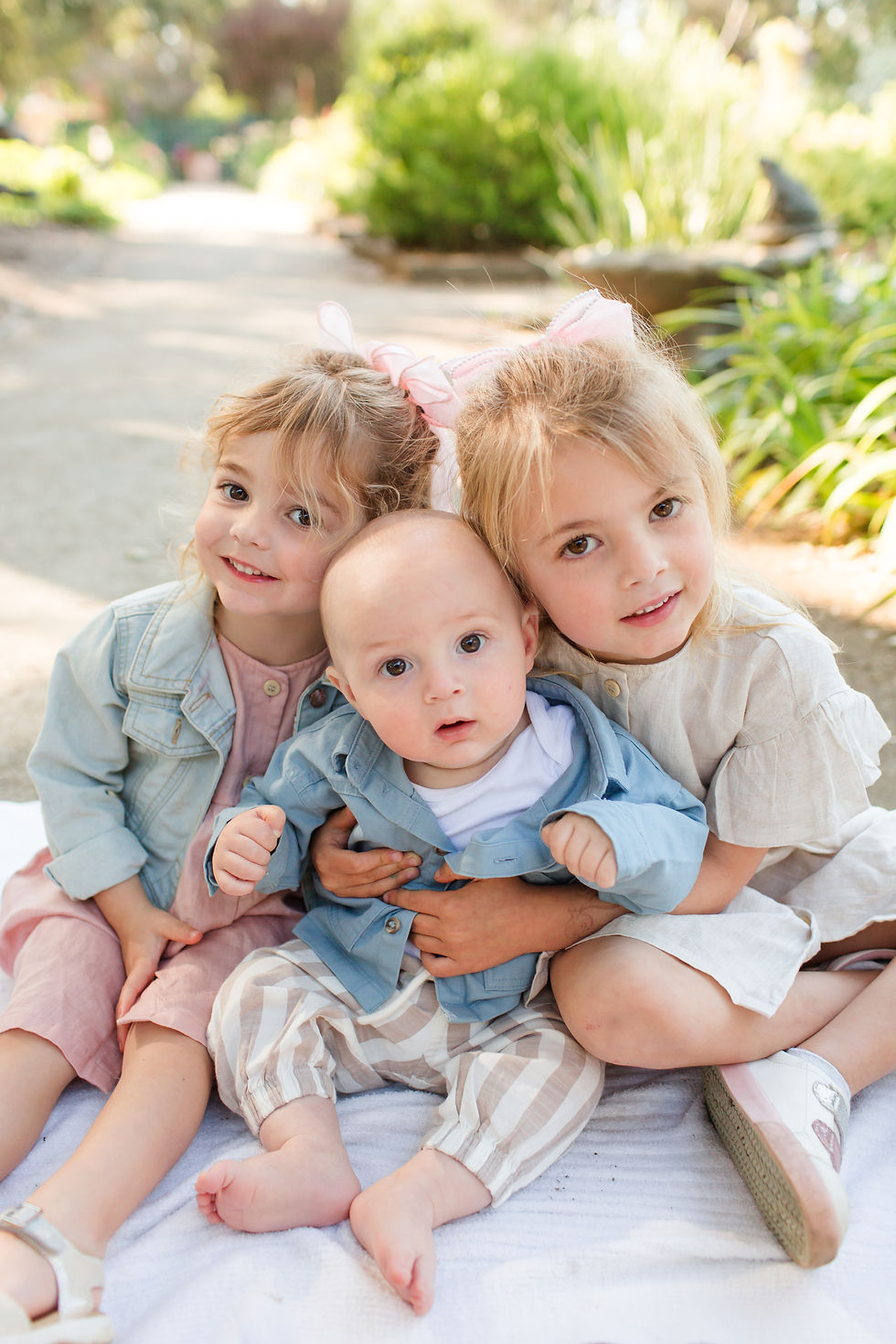 Three young children cuddle on a blanket in a sunny garden, smiling at the camera in soft pastel clothes.
Spring Family Photoshoot at Elizabeth Gamble Garden, Palo Alto by Bay Area Photographers HKCreate