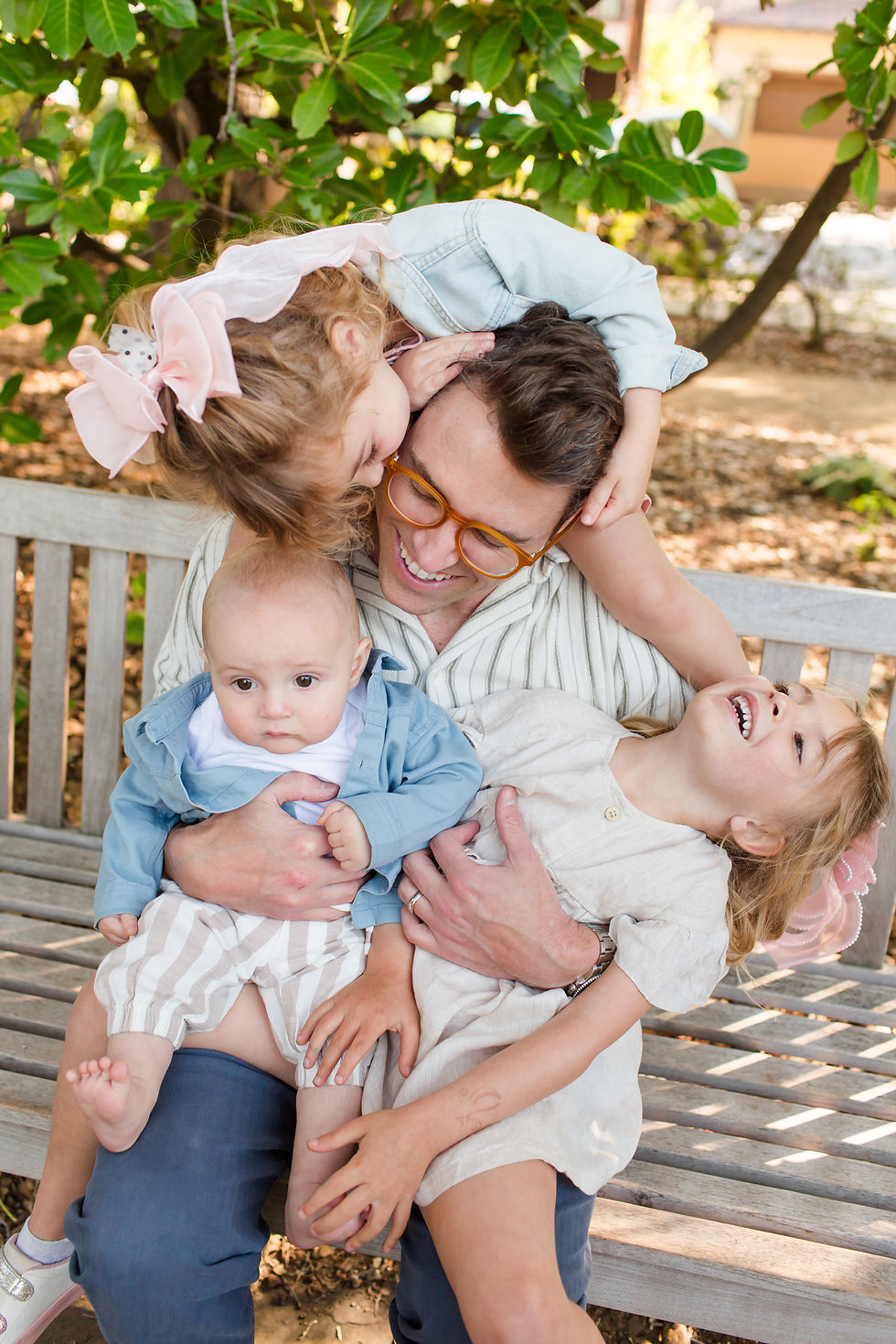 Smiling father on a bench hugs three young children outdoors under green trees, with one girl kissing his head and babies in his arms
Spring Family Photoshoot at Elizabeth Gamble Garden, Palo Alto by Bay Area Photographers HKCreate