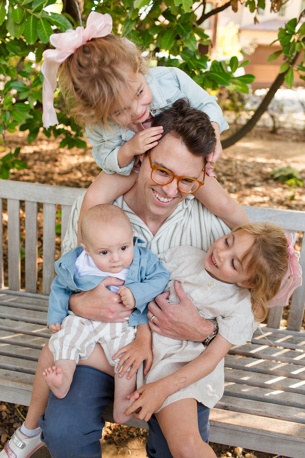 Smiling man with orange glasses sits on a bench outdoors, holding two children while a girl hugs his shoulders.
Spring Family Photoshoot at Elizabeth Gamble Garden, Palo Alto by Bay Area Photographers HKCreate