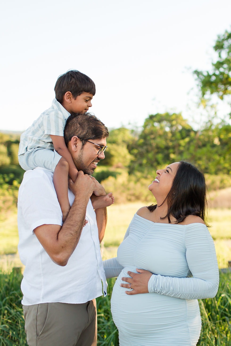 Father with child on shoulders, smiling at pregnant partner in light dress, outdoors. Greenery in background, joyful mood.
Spring Family Maternity Photoshoot at Pearson-Arastradero Preserve, Palo Alto by HKCreate Bay Area Photographers 