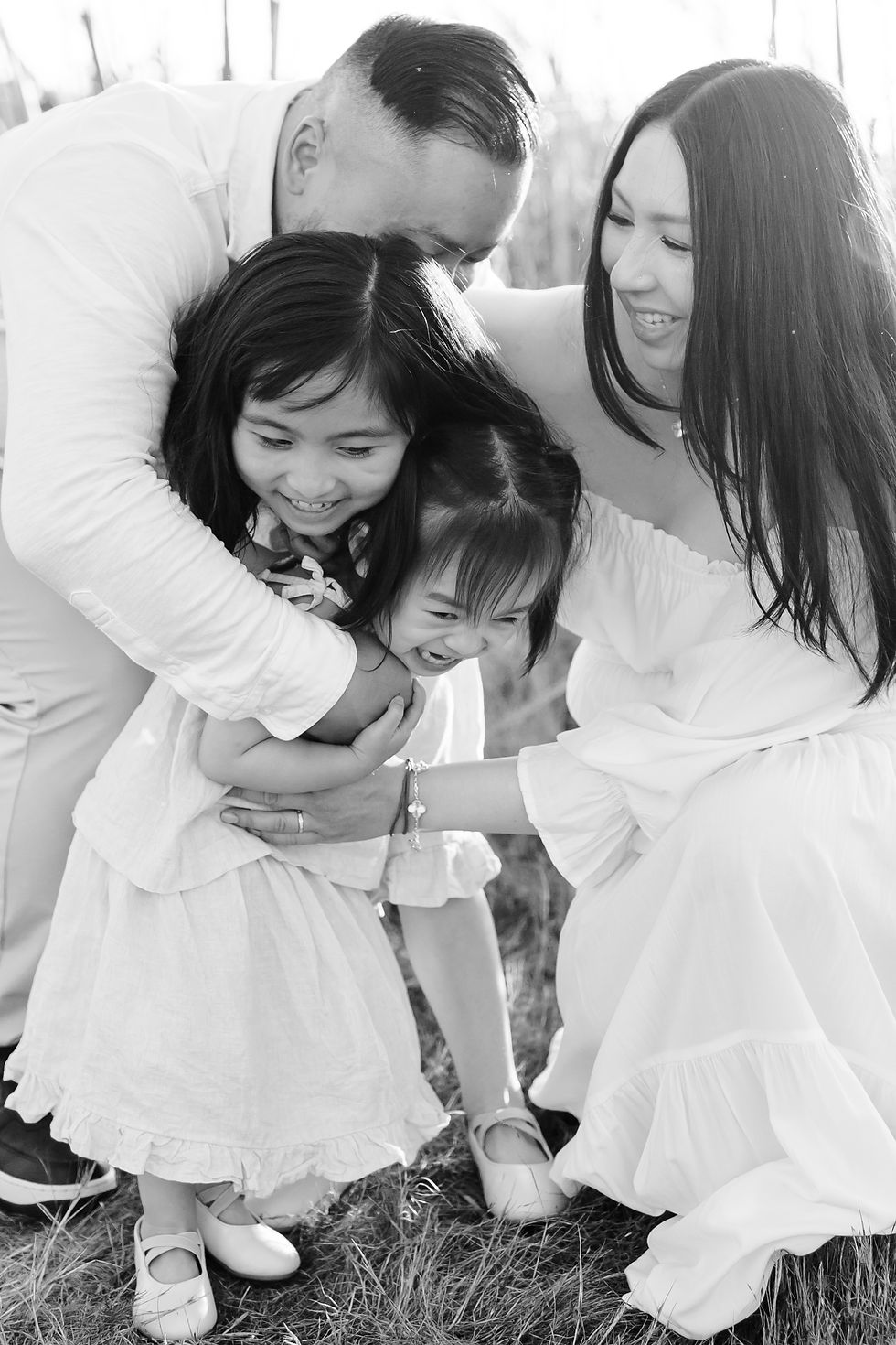 Family group hug in a grassy field, two parents and two young children smiling. Everyone is dressed in light clothing, creating a joyful mood.
Rockaway Beach, Pacifica Golden Hour Maternity Family Photoshoot by HKCreate Bay Area Photographers