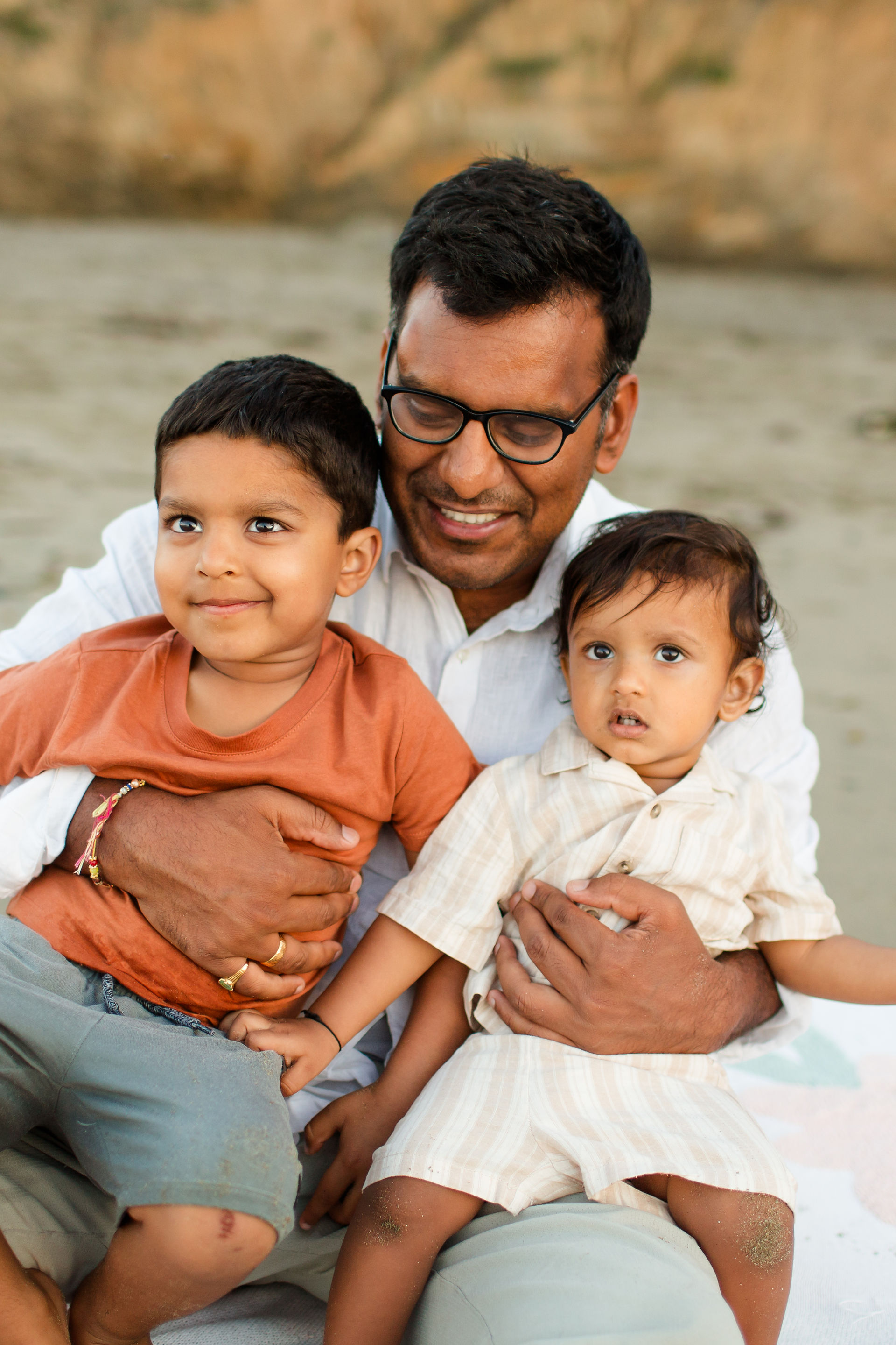 Dad holding young sons on the beach sitting on the sand. Rockaway Beach Pacifica Fun Playful and Cute Family Photoshoot by HKCreate Bay Area Photographers.