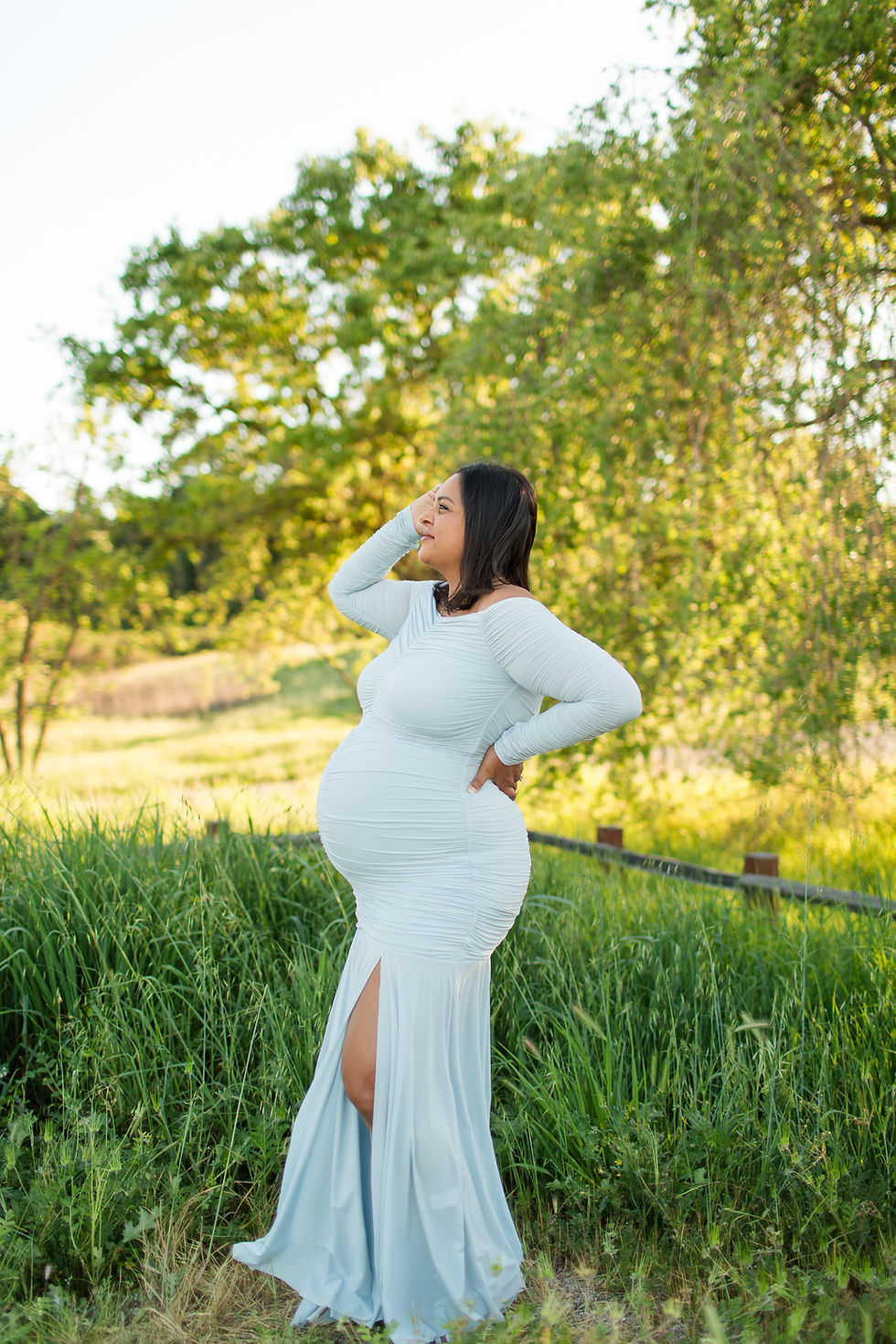 Pregnant woman in a white dress stands in a grassy field, hand on hip, smiling. Sunlight filters through green trees, creating a serene mood.
Spring Family Maternity Photoshoot at Pearson-Arastradero Preserve, Palo Alto by HKCreate Bay Area Photographers 