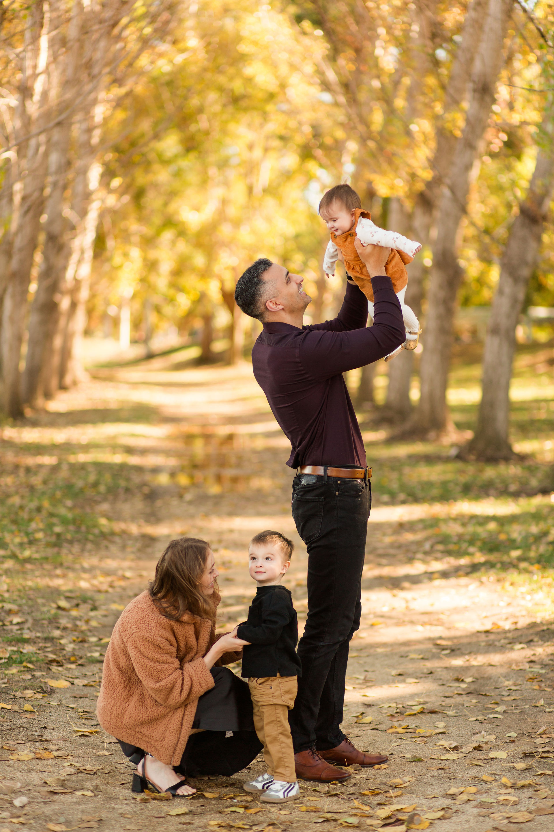 hkcreate bay area photography joyful candid light and airy san jose photographers northern california fall family of four photoshoot mom dad with two little kids boy and girl sweet hugging cute mustard yellow tan black outfits baylands park sunnyvale parents playing with kids
