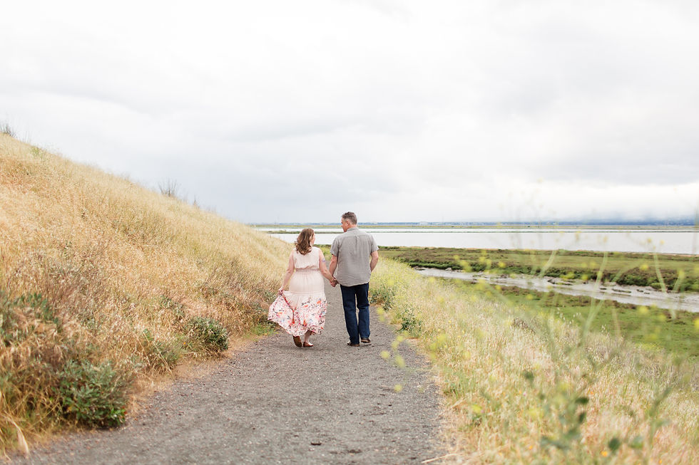 Couple holding hands, walking on a dirt path by a grassy hill and river, overcast sky. Woman in floral dress, man in gray shirt. Romantic mood.
Don Edwards San Francisco Bay National Wildlife Refuge, Fremont Couple Photoshoot by HKCreate Bay Area Photographers