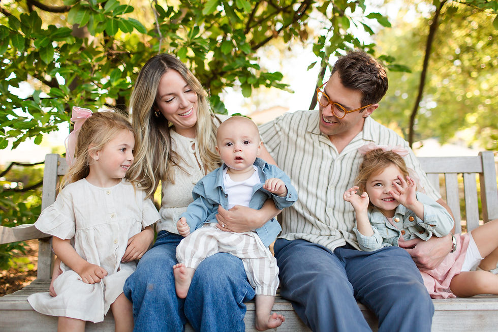 Smiling family of five sitting on a wooden bench outdoors under leafy trees, with two young girls and a baby.
Spring Family Photoshoot at Elizabeth Gamble Garden, Palo Alto by Bay Area Photographers HKCreate