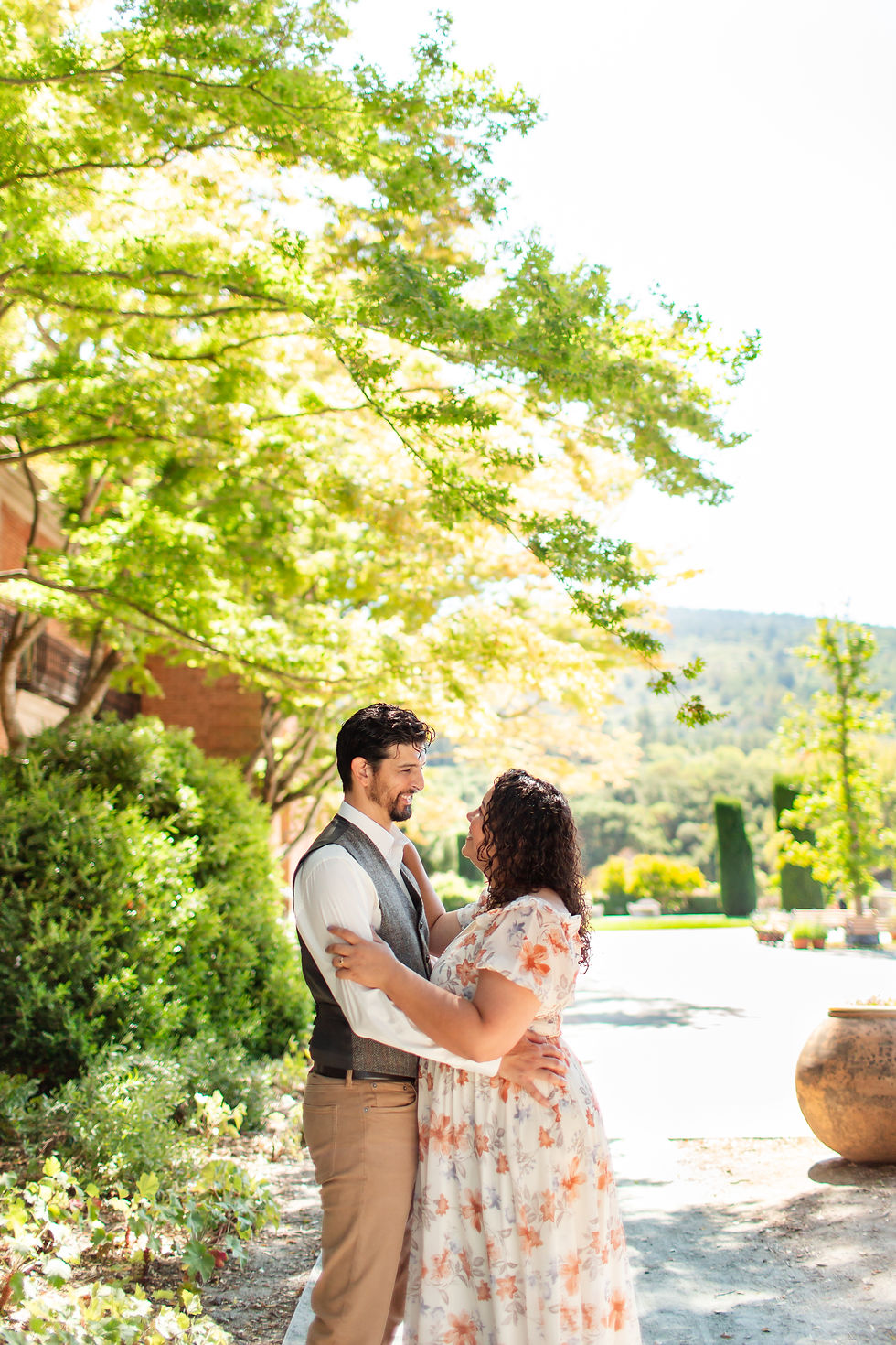 A couple embraces under sunlit trees in a garden setting. She wears a floral dress; he wears a vest. The mood is joyful and serene.
Filoli Historic House and Garden Woodside, California Couple Photoshoot by HKCreate Bay Area Photographers