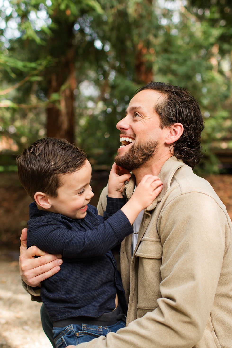 Smiling man holds a young boy in a forest, while the boy reaches for his beard; warm, joyful moment with green trees
Winter Family Maternity Photoshoot at Redwood Grove Nature Preserve, Los Altos by Bay Area Photographers HKCreate