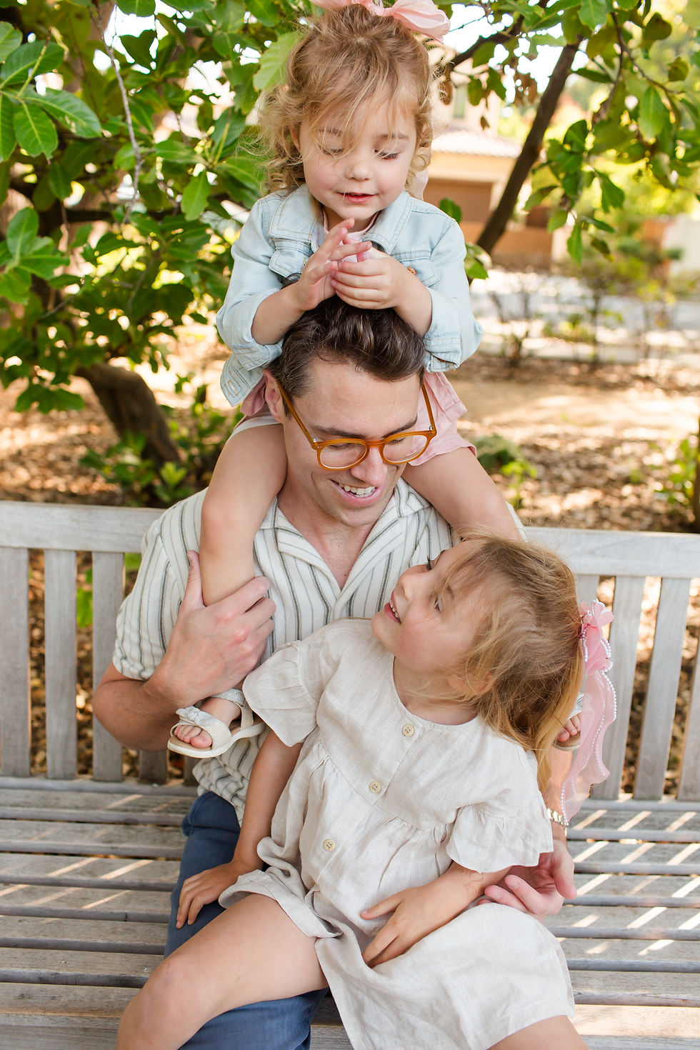 Smiling father sits on a bench while two little girls hug him outdoors under leafy trees.
Spring Family Photoshoot at Elizabeth Gamble Garden, Palo Alto by Bay Area Photographers HKCreate