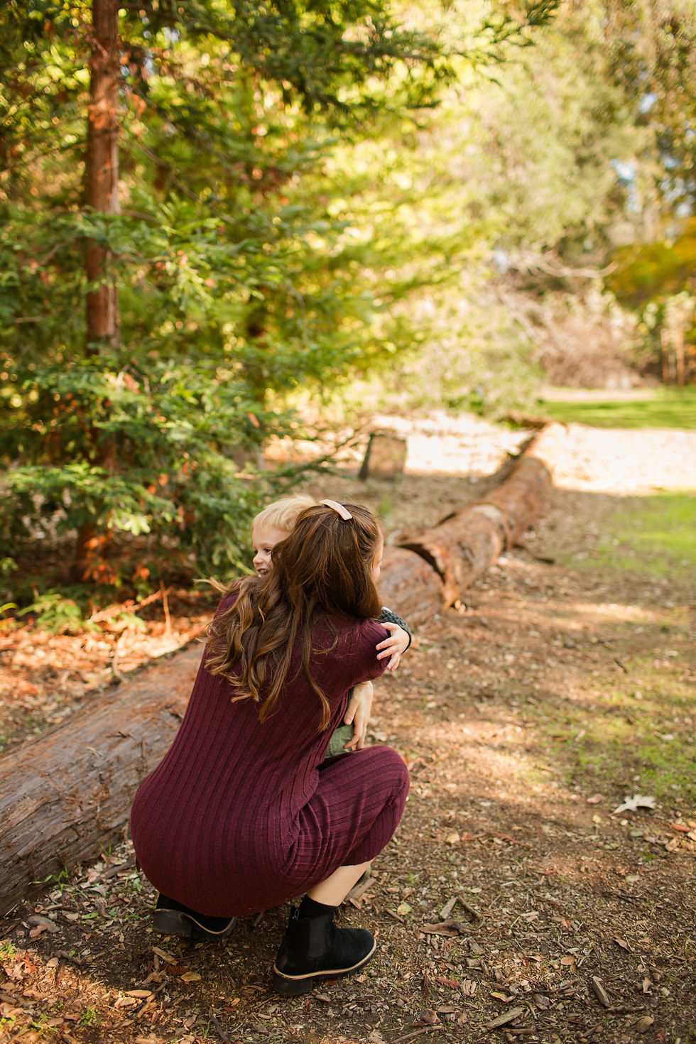 Woman in a maroon dress hugging a child in a forest setting. Sunlight filters through trees, creating a warm, peaceful mood.
Winter Family Session at Redwood Grove Nature Preserve in Los Altos by Bay Area Photographers HKCreate