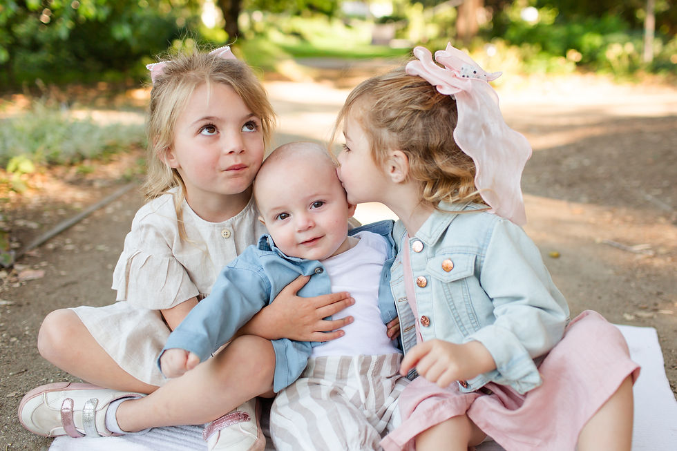 Three small children sit on a path in a sunny park, one girl kissing a baby on the head while another holds him close.
Spring Family Photoshoot at Elizabeth Gamble Garden, Palo Alto by Bay Area Photographers HKCreate