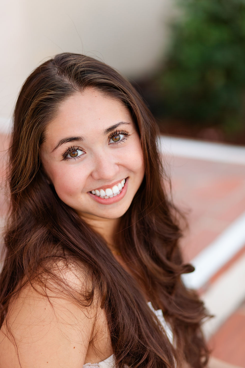 Smiling young woman with long brown hair in a soft-focus outdoor portrait, against blurred green and pink background.
Santa Clara University Grad Photoshoot by Bay Area Photographers HKCreate
