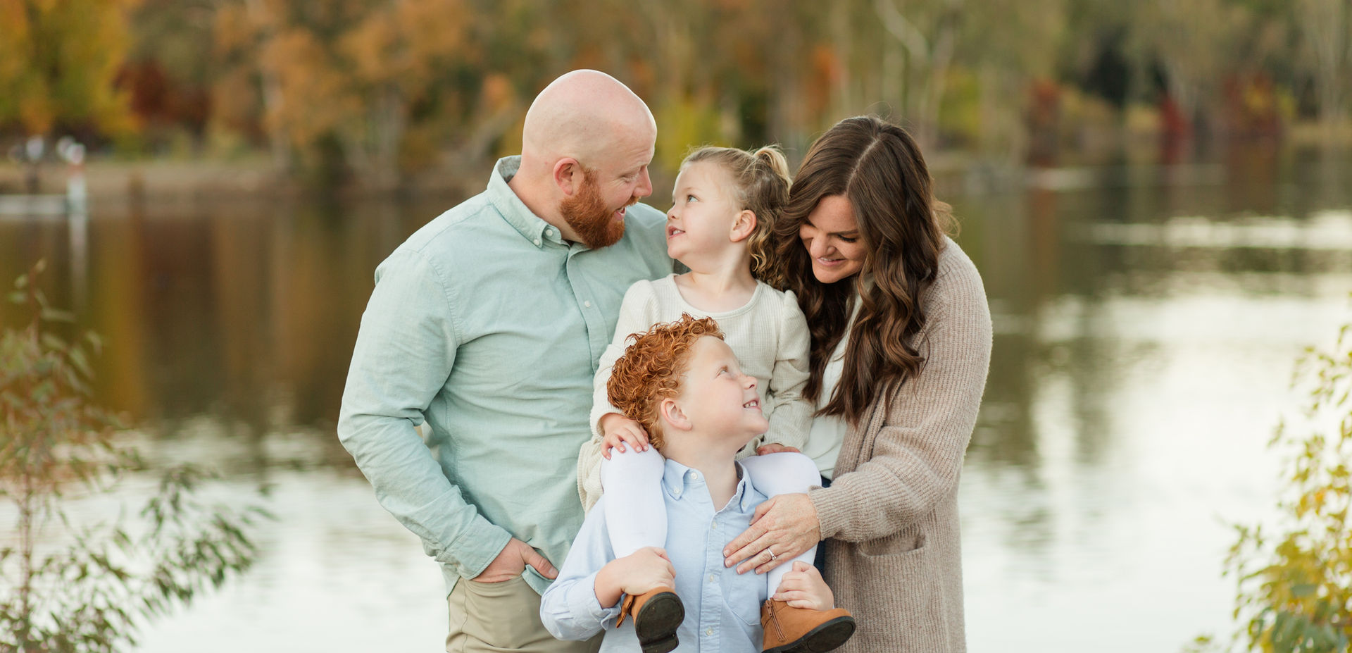 family of four looking at each other smiling with sister on brothers shoulders hkcreate