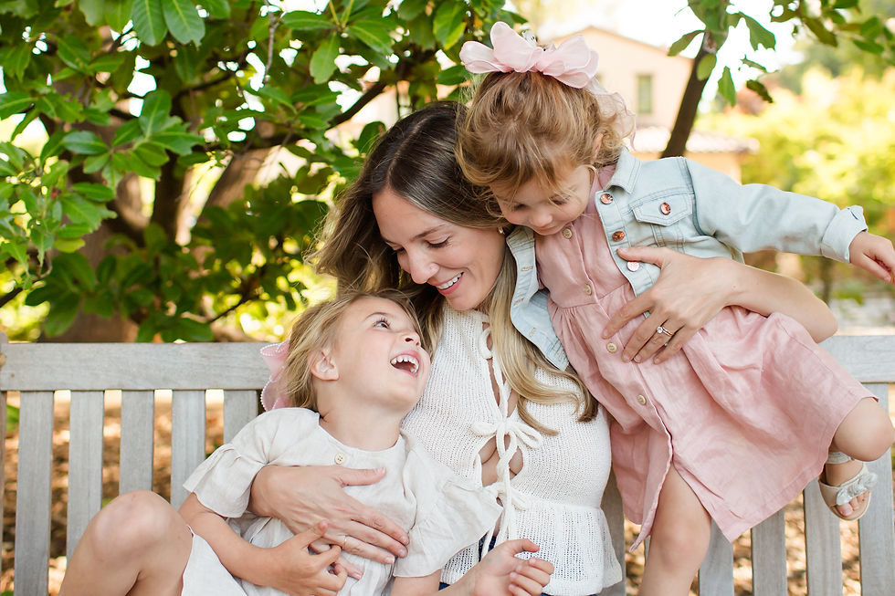 Smiling mother hugs two young daughters on a bench under leafy trees, in soft daylight, wearing pink and white outfits.
Spring Family Photoshoot at Elizabeth Gamble Garden, Palo Alto by Bay Area Photographers HKCreate