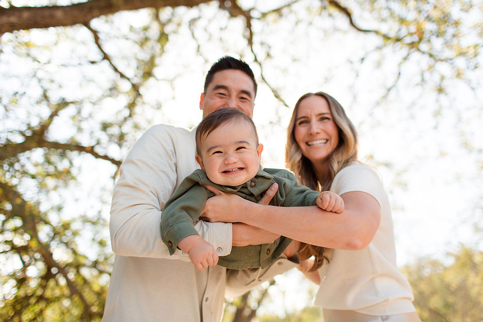 Smiling family of three outdoors; baby in green held by parents. Sunlit trees in background, creating a warm, joyful mood.
One year old birthday boy legacy fall family photoshoot at Guadalupe Oak Grove Park, San Jose by HKCreate Bay Area Photographers.