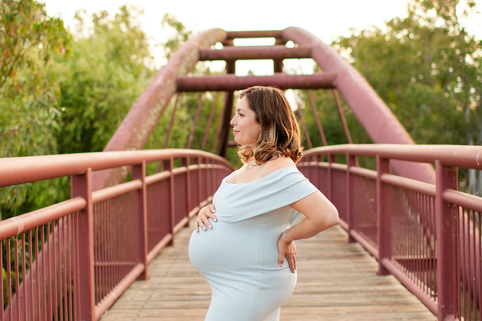 Pregnant woman in a light blue dress stands on a rustic red bridge, hands on her belly, surrounded by lush green trees at sunset.
Vasona Lake Park, Los Gatos Maternity Summer Family Photoshoot by Bay Area Photographers HKCreate.