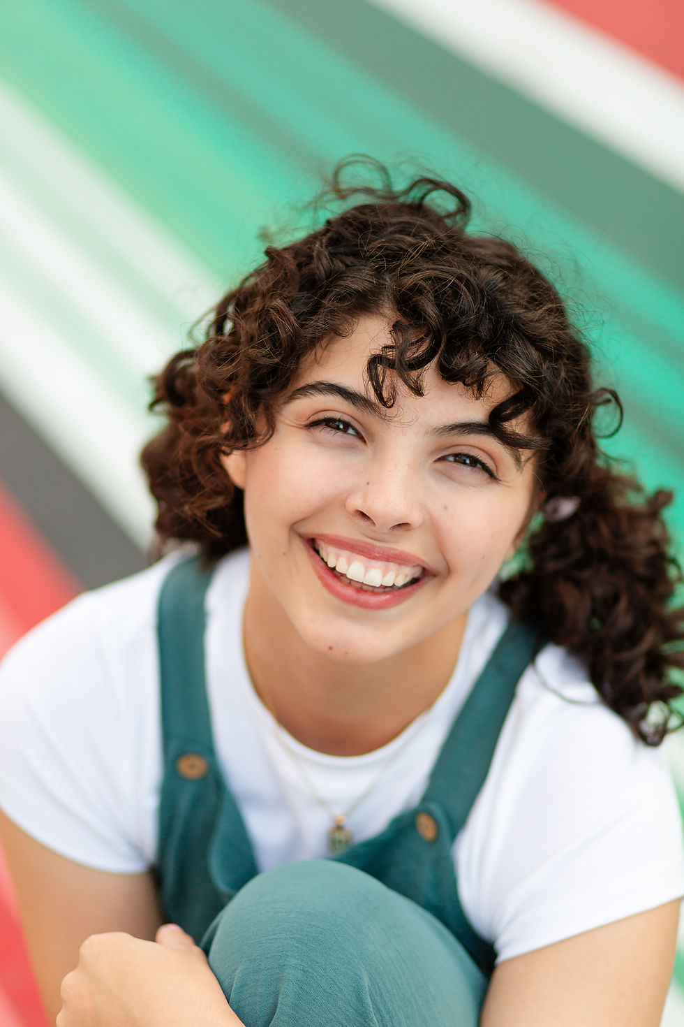 Smiling curly-haired young woman in teal overalls and white shirt, seated against a colorful striped background.
Spring High School Grad Photoshoot Downtown San Mateo  by Bay Area Photographers HKCreate