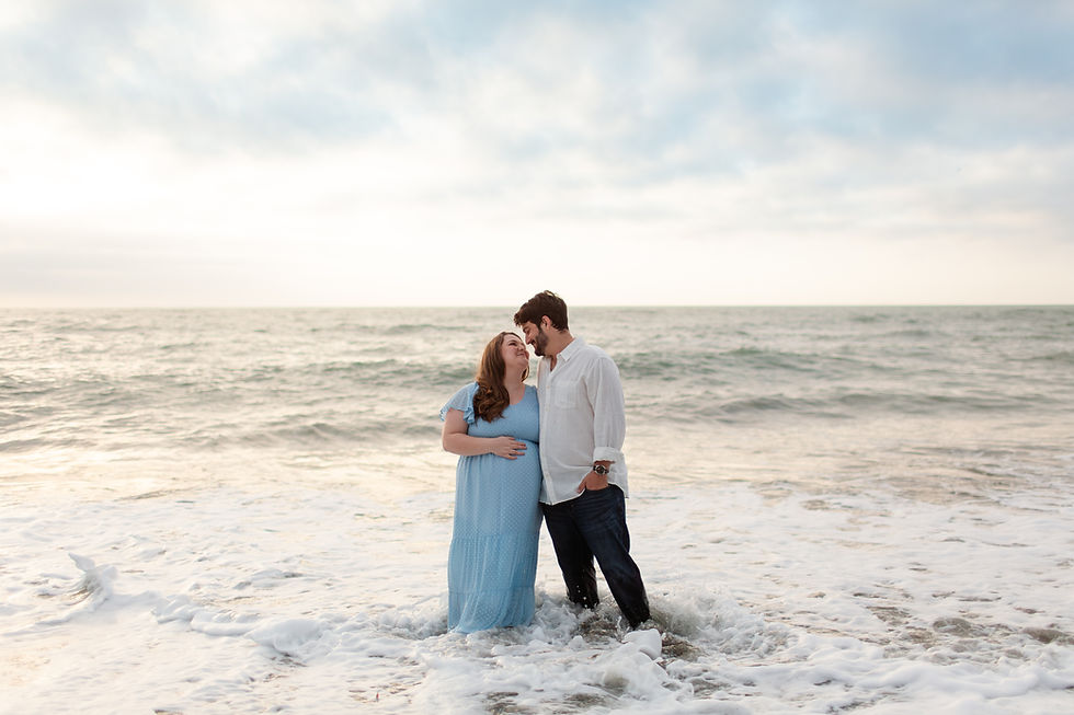 Couple standing in ocean waves at sunset. Woman in blue dress cradles her belly, smiling. Man in white shirt gazes at her lovingly.
Rockaway Beach, Pacifica spring maternity photoshoot by Bay Area Photographers HKCreate