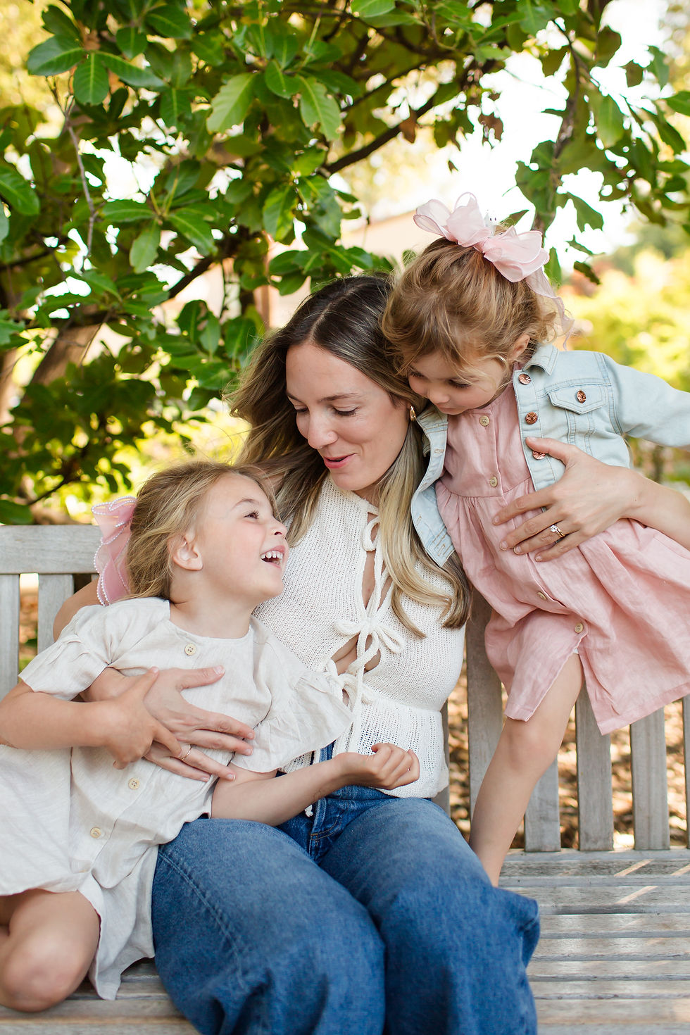 Mother with two young daughters on a bench under green trees, smiling and cuddling in soft pink and white outfits.
Spring Family Photoshoot at Elizabeth Gamble Garden, Palo Alto by Bay Area Photographers HKCreate