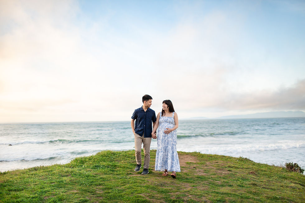 A couple walks hand in hand on a grassy cliff by the sea at sunset. They are smiling, with a peaceful ocean and pastel skies in the background.
Sunset Spring Beach Maternity Session at Rockaway Beach in Pacifica by HKCreate Bay Area Photographers