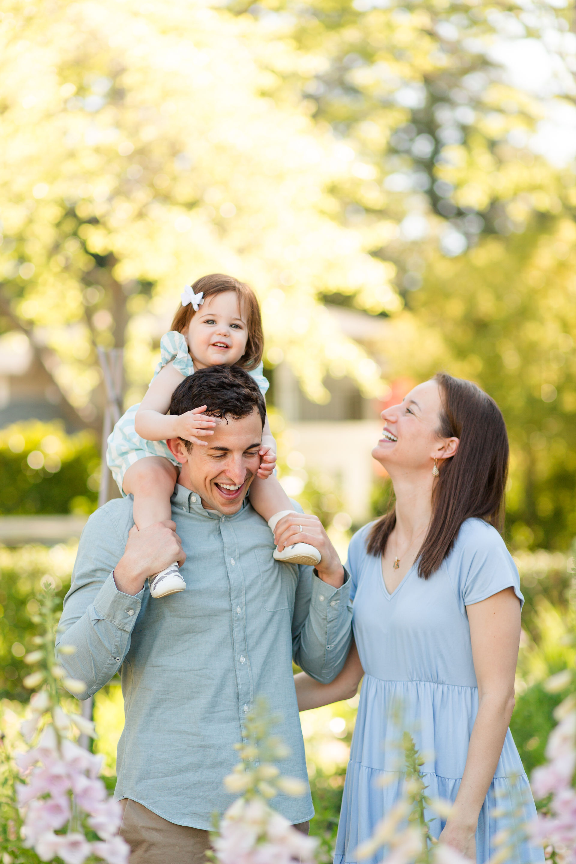 hkcreate bay area photography joyful light and airy san jose photographers northern california photoshoot spring family of three toddler girl baby blue striped dress outfit ideas gamble garden palo alto daughter on shoulders purple pink flowers laughing
