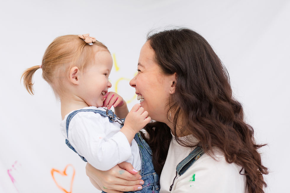 Woman holds a smiling toddler in denim overalls against a white backdrop with colorful heart drawings, evoking joy and warmth.
Mommy and Me Maternity Outdoor Painting Session by HKCreate Bay Area Photographers at Guadalupe Oak Grove Park in San Jose