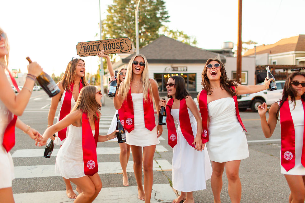 Group of women in white dresses and red sashes celebrating outdoors. They hold bottles and a "Brick House" sign, smiling and joyful.
Santa Clara University graduation group photoshoot at the Hut on campus. Girls having fun. Bay Area Photographers HKCreate