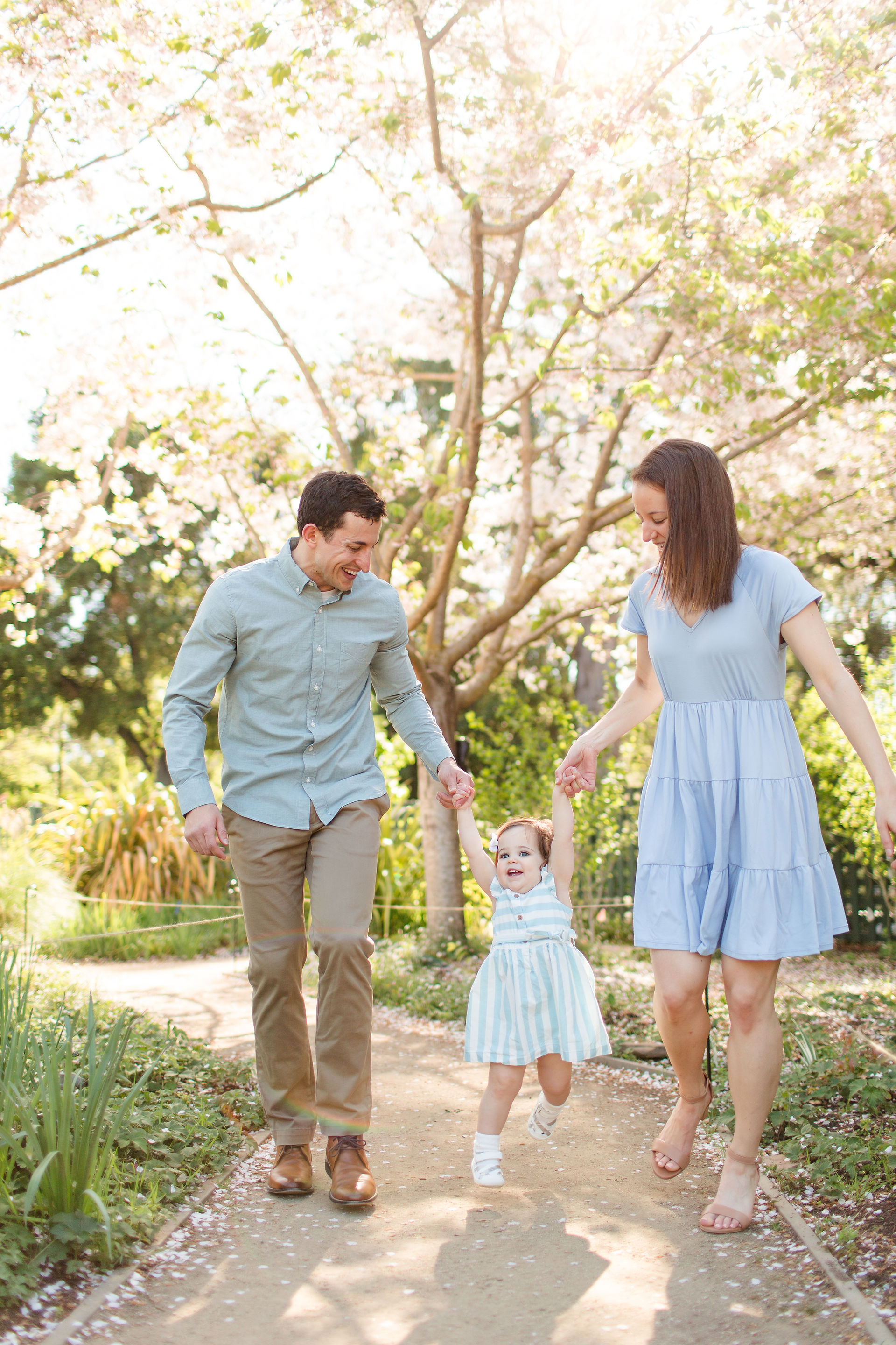 hkcreate bay area photography joyful light and airy san jose photographers northern california photoshoot spring family of three toddler girl baby blue striped dress outfit ideas gamble garden palo alto swinging in the air under blooming trees