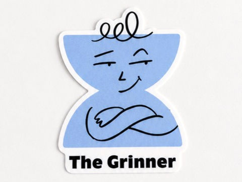 A cut out sticker of the Grinner character. Light blue hourglass shape with the word The Grinner curved up the side