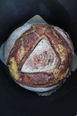 A large, round loaf of sourdough with bits of golden polenta peaking through the scores
