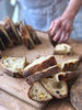 Several pieces of sourdough, freshly cut, in the foreground, with hands cutting more slices in the background.