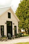 A white-washed board and batten building with black trim and a black sign that says 'Red Hen Artisanale'. The studio has 4 blue muskoka chairs out front. Priceville, ON