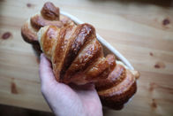A hand holding a golden-baked sourdoughcroissant above a wooden table.