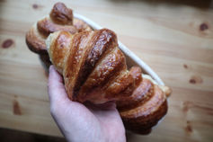 A hand holding a golden-baked sourdoughcroissant above a wooden table.