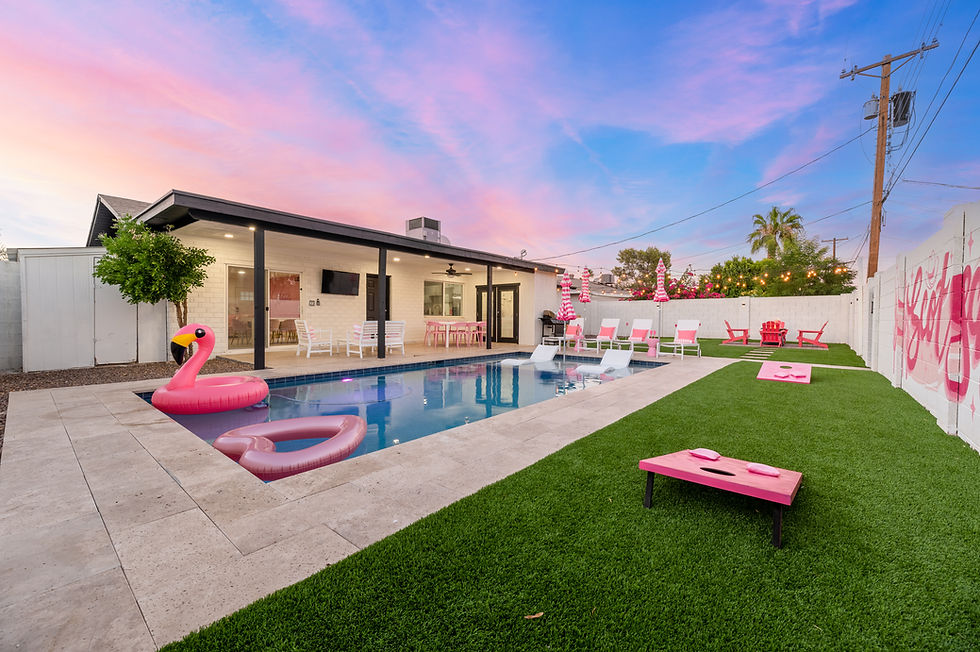 Private pool with a pink flamingo float, surrounded by a grassy lawn, patio furniture, and a pink cornhole game