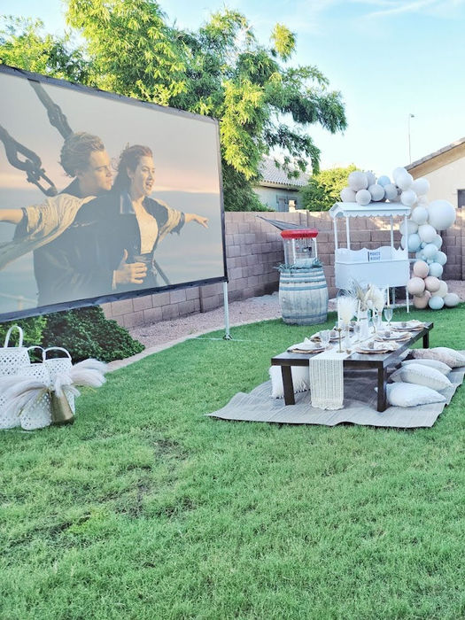 Outdoor movie night setup with a large screen showing a movie, a picnic table, and seating for guests.