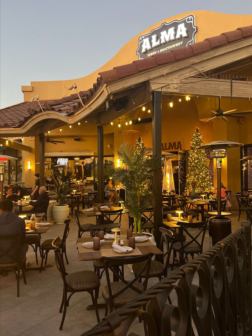 Outdoor patio dining at ALMA Scottsdale, featuring tables, chairs, and a festive Christmas tree.