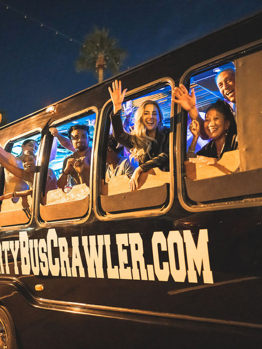Group of friends in a party bus, waving from the windows with Scottsdale Party Bus Crawler.com on the side of the bus
