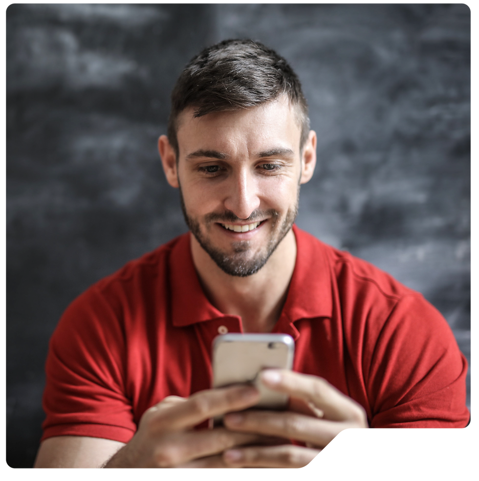 Smiling man in a red polo looks down at his smartphone against a blurred gray background, represents a Zoek Marketing client.