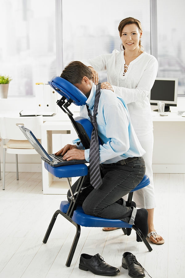 Professional massage therapist massaging a client's back while the client sits in a portable massage chair.