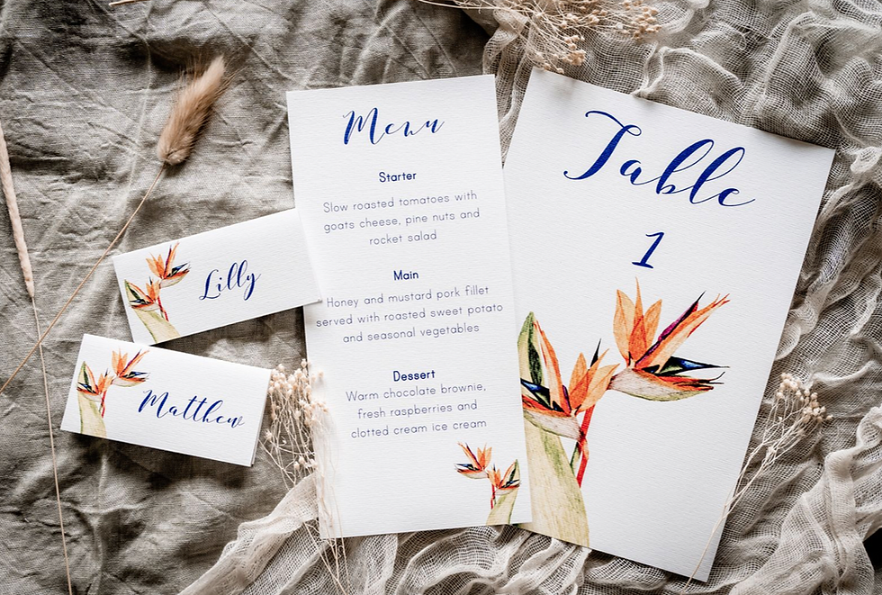 on the day wedding stationery laid out with hand painted bird of paradise flower. place cards, menu and table number