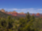 Red rock formations under a clear blue sky with green trees in the foreground, creating a vibrant desert landscape.