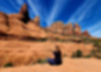 Hiker sitting on red rock, gazing at Sedona's rugged cliffs under a bright blue sky. Tranquil, natural setting with stunning formations.