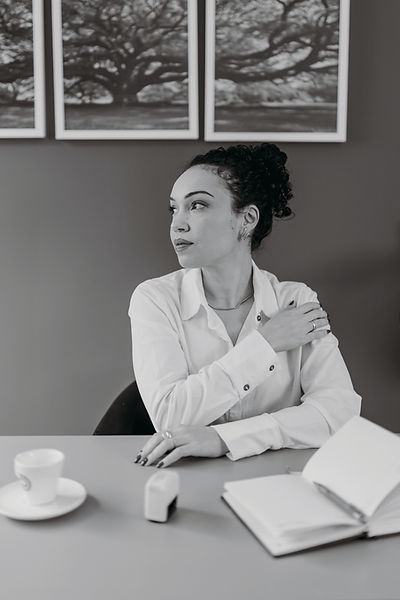 Dra. Fernanda sentada em mesa de escritório e olhando para o lado esquerdo. Ela veste uma camisa branca.