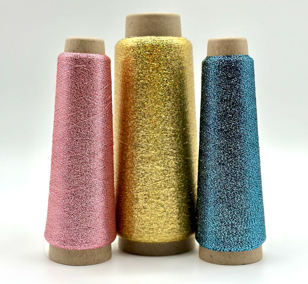 Three cones of sparkling thread in pink, gold, and blue stand side by side against a plain white background, creating a vibrant display.