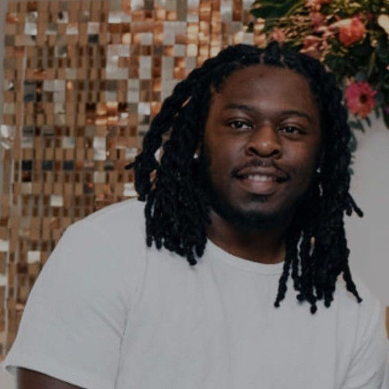Man with long dark dreadlocks smiling in a white t-shirt