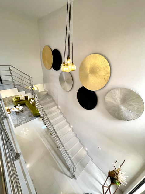 Escaleras en vista contra picada. Candil colgante. Accesorios de pared gigantes, circulares, plateado, negro y dorado. Pareces y piso blancos. 