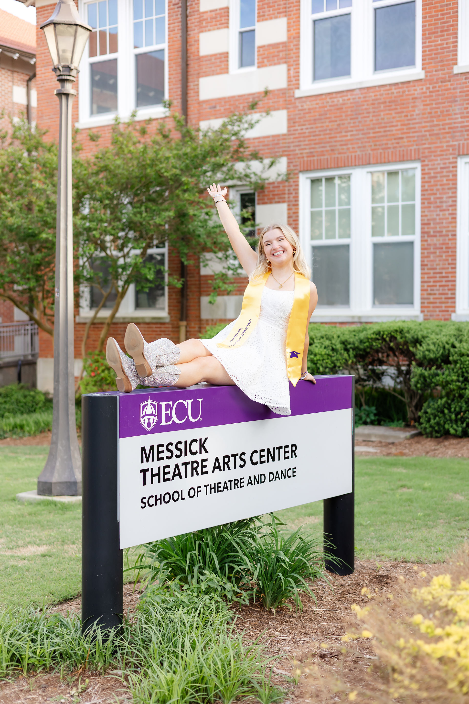 ECU senior sitting on Messick Theatre sign at East Carolina University campus.