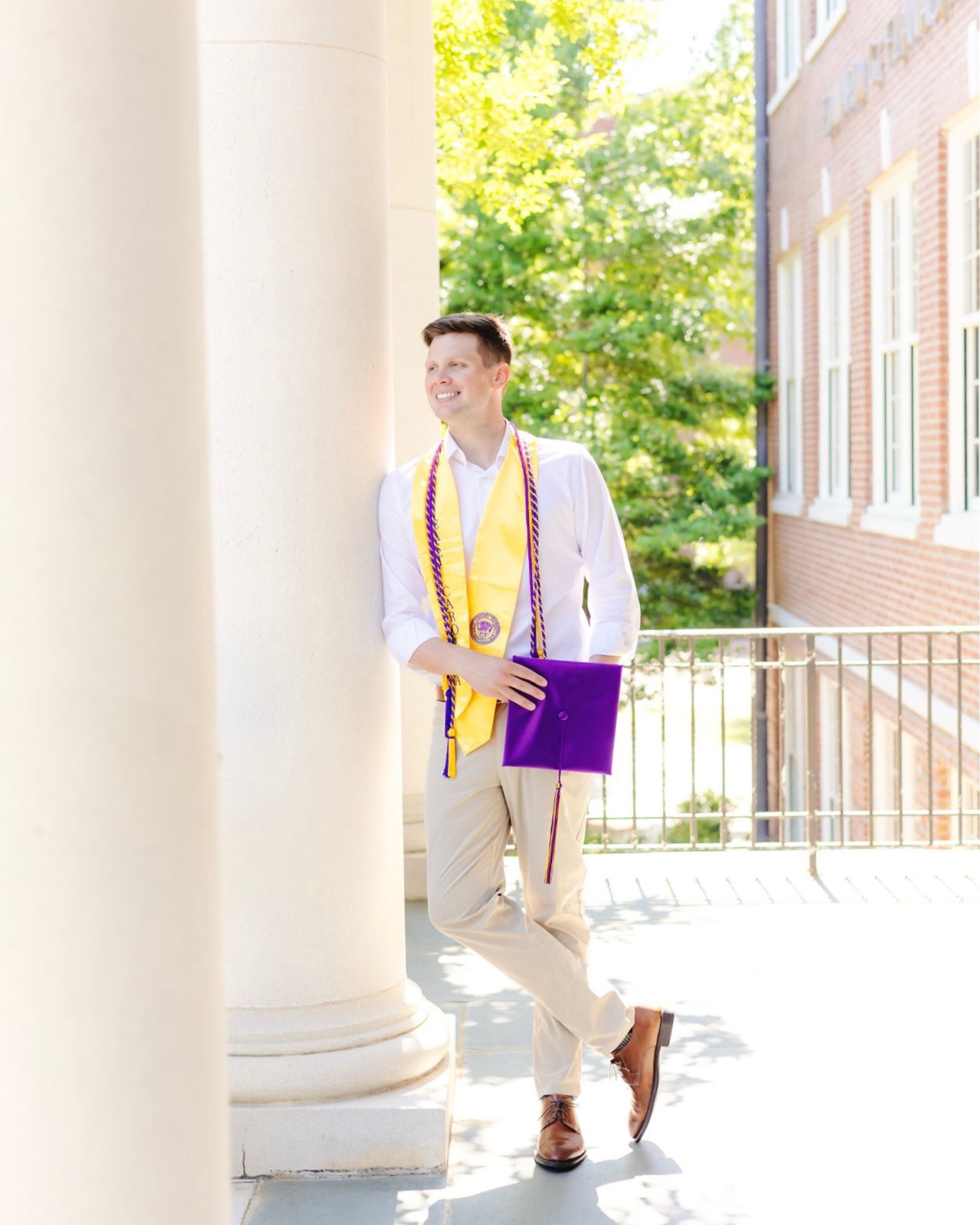 Male ECU senior posing near Flanagan building columns holding graduation cap in Greenville NC.